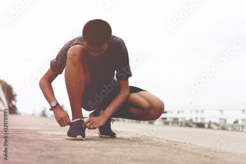 Tie a shoe,Asian male jogger athlete training and doing workout outdoors on a street, He tying laces for jogging on road with running shoes. Runner getting ready for exercise. Sport lifestyle concept