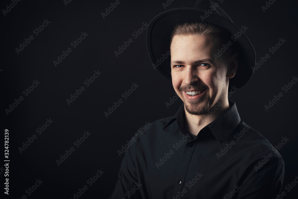 Portrait of smiling guy with chintuft wearing black shirt and fedora hat looking at camera, isolated Portrait of smiling guy with chintuft wearing black shirt and fedora hat looking at camera, isolated