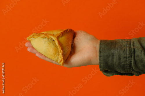 Echpochmak Tatar traditional dish. Echpochmak in hand on an orange background. Traditional food, quick snack of dough.  photo