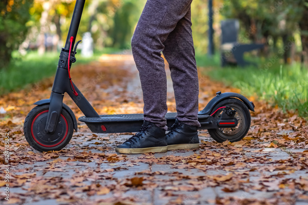 Obraz premium Woman is staying on electric scooter in autumn park. Active lifestyle. Modern ecologic transport. Modern city lifestyle.