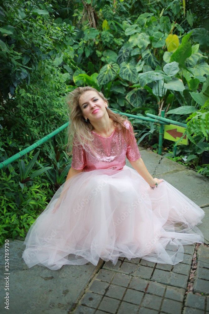 Fototapeta premium beautiful white long hair girl in a tropical garden in a light tulle pink skirt