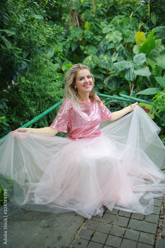 Fototapeta premium beautiful white long hair girl in a tropical garden in a light tulle pink skirt