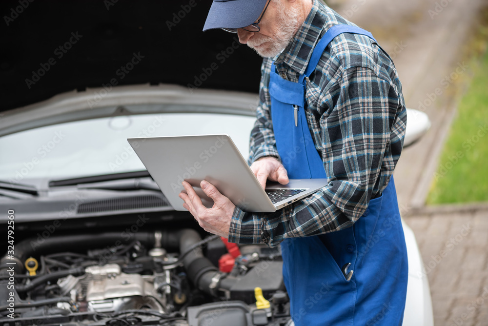Mechanic using laptop for checking car engine Mechanic using laptop for checking car engine