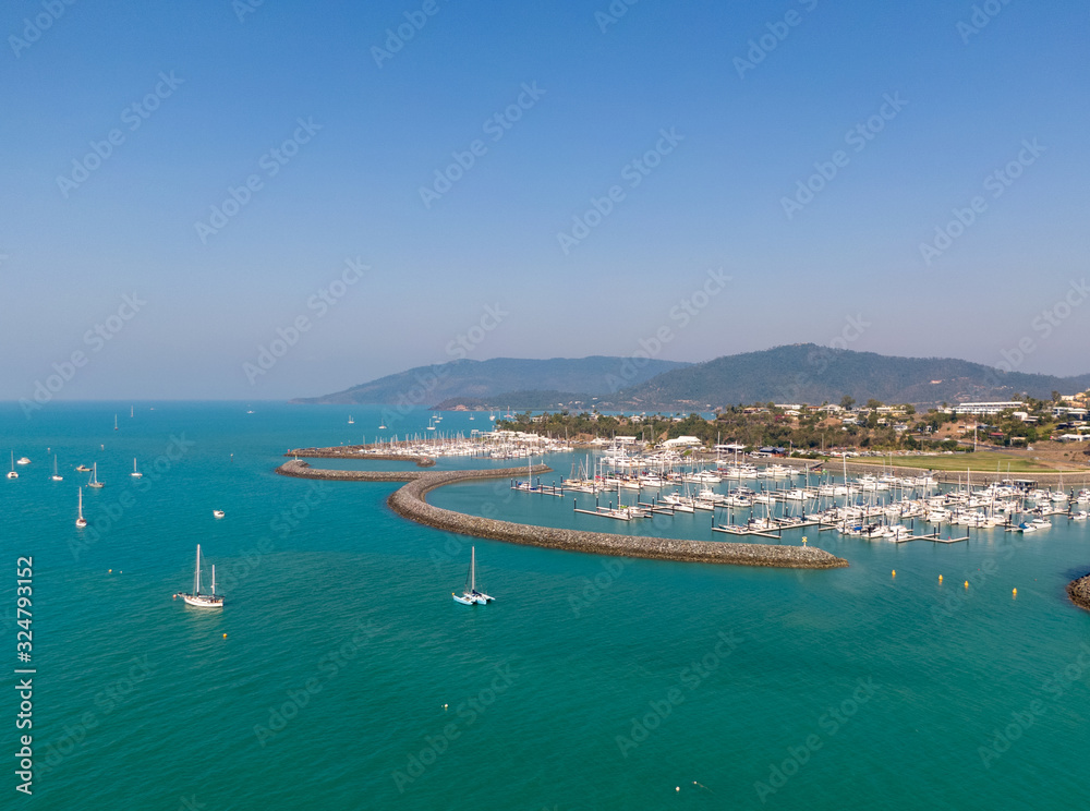 Panoramic marina town aerial. Airlie beach waterfront aerial view. Dramatic DRONE view from above. Marina town with yachts and boats in sea water. Mountain landscape background. Whitsundays Islands