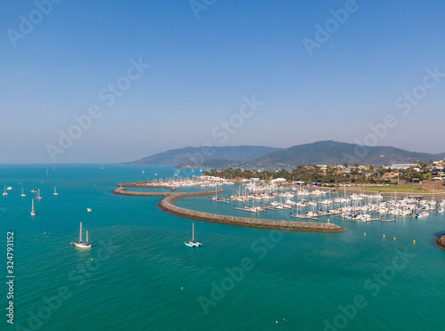 Panoramic marina town aerial. Airlie beach waterfront aerial view. Dramatic DRONE view from above. Marina town with yachts and boats in sea water. Mountain landscape background. Whitsundays Islands