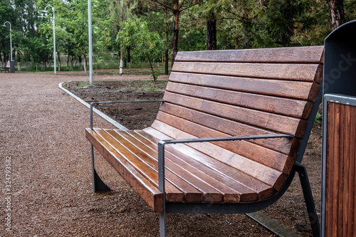 New brown wooden bench and trach bin in a park with rain drops on them. Park after rain. photo