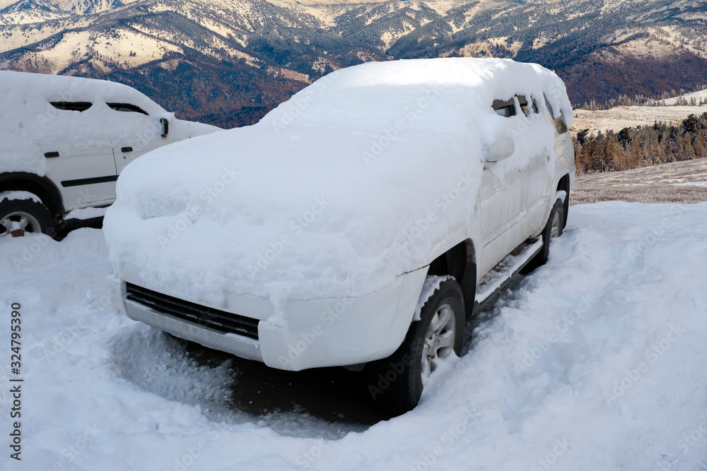 Car covered with snow after snowfall with mountains background. SUV in mountains after blizzard. Car covered with snow after snowfall with mountains background. SUV in mountains after blizzard.
