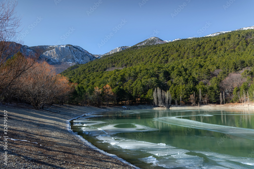Mountain turquoise lake in Crimea in winter; winter landscape with forest and lake Mountain turquoise lake in Crimea in winter; winter landscape with forest and lake