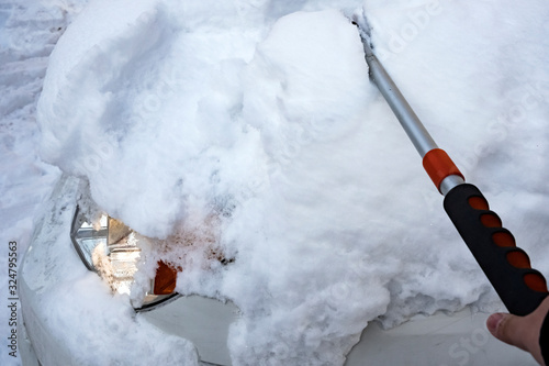 Cleaning car with brush after snowfall. Cold weather. Snow removing from car after blizzard.