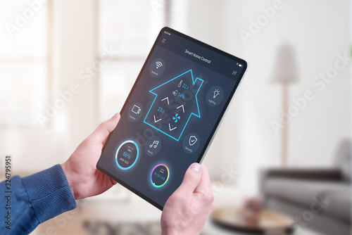 Concept of smart home central control system app on tablet in man hands. Home interior in background