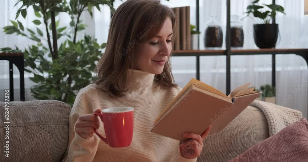 Happy woman reading a book and drinking coffee on sofa at home Happy woman reading a book and drinking coffee on sofa at home