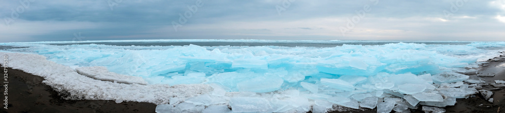 Obraz premium Panoramic landscape of frozen lake. Cracked ice on lake in winter season, natural landscape background.