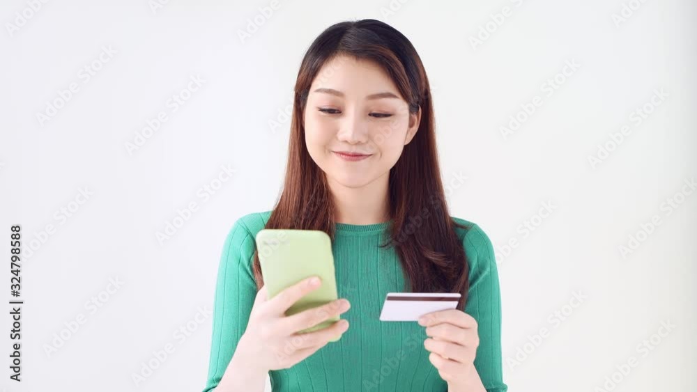 Portrait of happy young woman shopping online and paying for purchases using credit card and smartphone isolated on light background Portrait of happy young woman shopping online and paying for purchases using credit card and smartphone isolated on light background