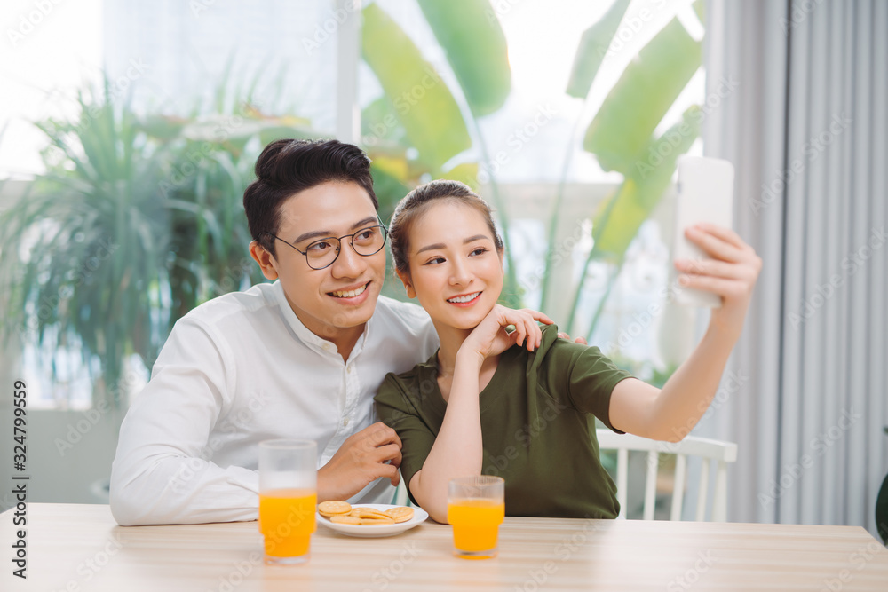 Beautiful young couple making selfie ,using a smart phone and smiling while sitting in their apartment