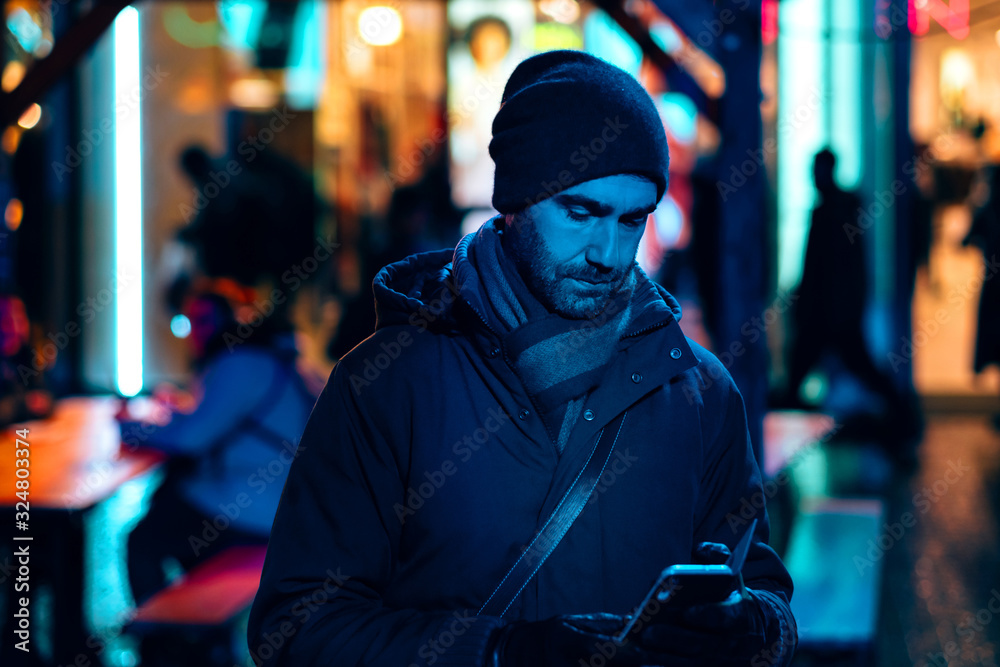 man outdoor at night in the city using a mobile phone surrounded by the neon sign lights