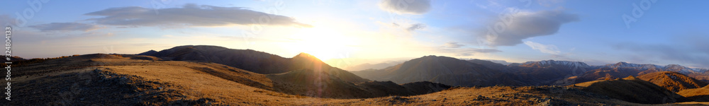 Panorama of beautiful sunrise in the mountains with cloudy sky and mountains silhoettes.