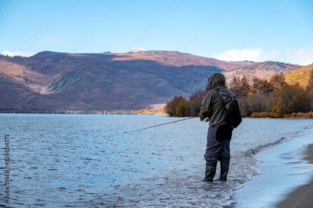 Fisherman with fiching rod on a lake in autumn. Man fisherman is catching a predator fish. Fisherman with fiching rod on a lake in autumn. Man fisherman is catching a predator fish.