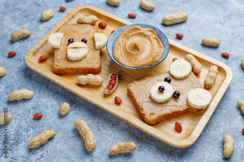 Funny bear and monkey face sandwich with peanut butter, banana and black currant,peanuts on grey concrete background,top view
