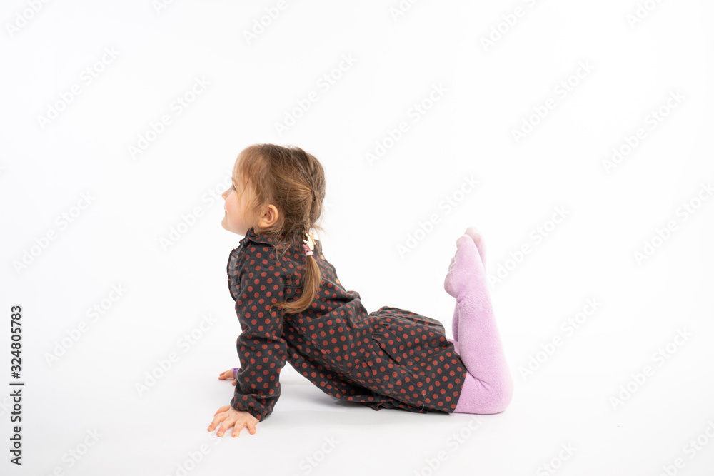 Little playfull girl in dress lying on the floor looking to the copy space area, isolated over white background Little playfull girl in dress lying on the floor looking to the copy space area, isolated over white background