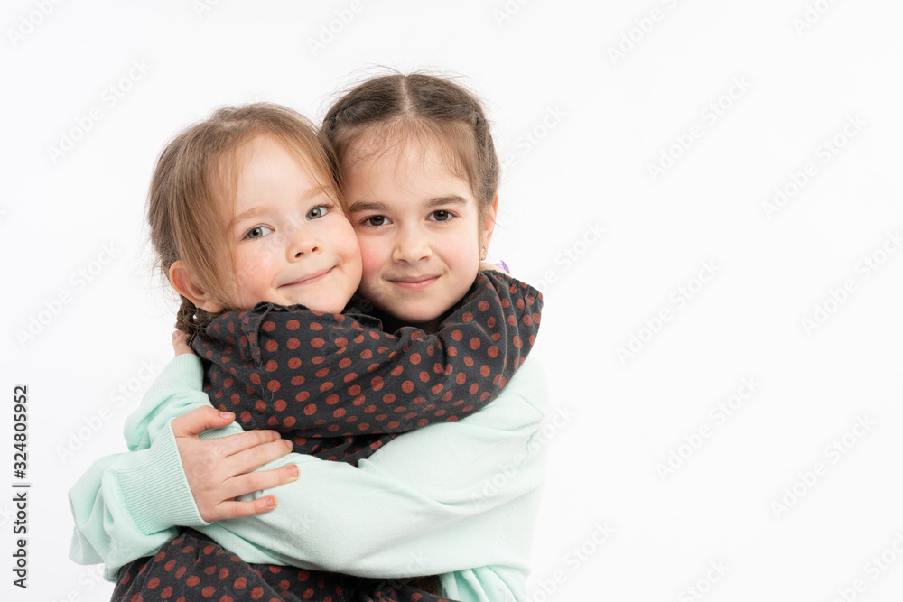 Lovely sisters in casual clothes hugging each other and looking at the camera, happy family concept, isolated portrait Lovely sisters in casual clothes hugging each other and looking at the camera, happy family concept, isolated portrait