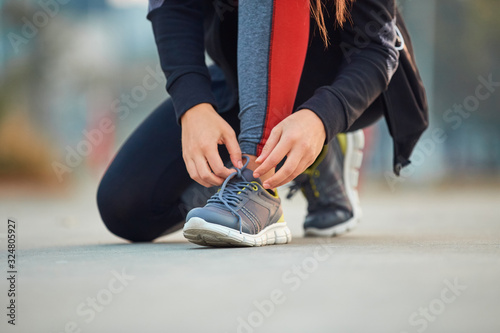 Sporty woman tying running shoes in urban park.