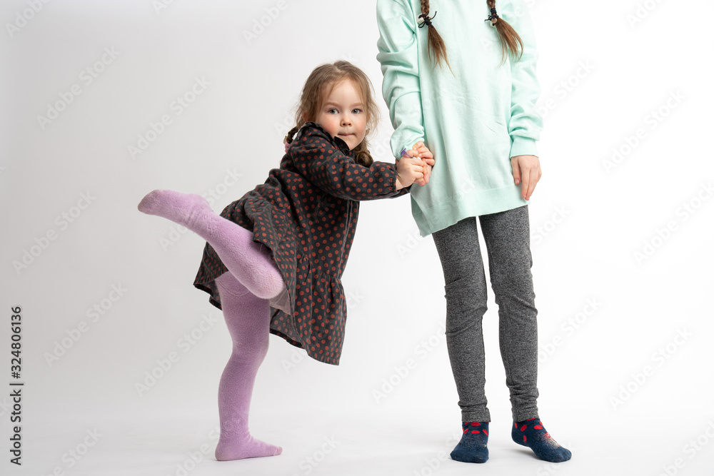 Funny little child girl in dress holds sister's hand and raises her leg ...