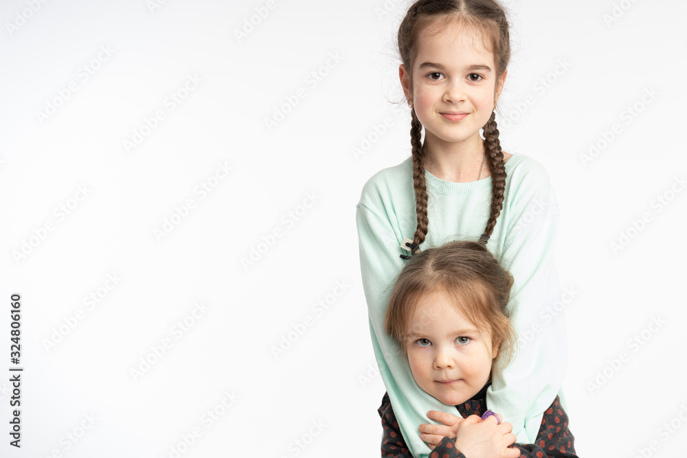 Beautiful little girls, child with pigtails hugging her little sister, both looking at the camera, isolated over white background Beautiful little girls, child with pigtails hugging her little sister, both looking at the camera, isolated over white background