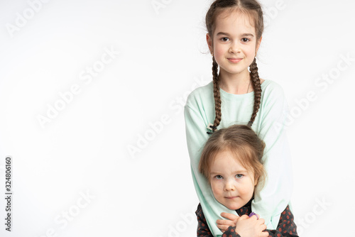 Beautiful little girls, child with pigtails hugging her little sister, both looking at the camera, isolated over white background © Vasya