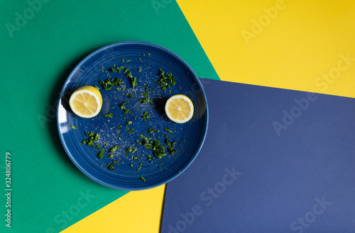 Plate with cut parsley and dill, sea salt, milled pepper, lenon on green, blue, yellow background photo