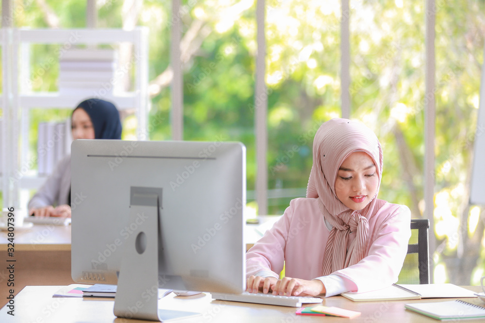 Beautiful Muslim woman was sitting intently at the computer screen in the office with another colleague. Beautiful Muslim woman was sitting intently at the computer screen in the office with another colleague.