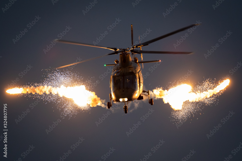 Military helicopter in flight firing off flare decoys at night. - obrazy, fototapety, plakaty 