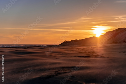 Sand blowing over sandy beach in wind with unfocused sand dunes. sea and sun background.