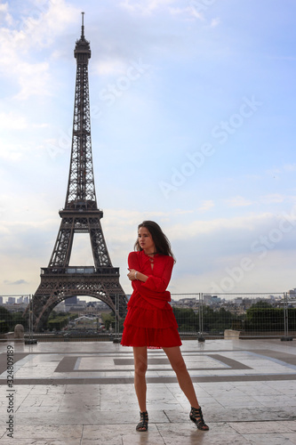 Beautiful young girl with long brown hair in red dress stay in front of Eiffel tower