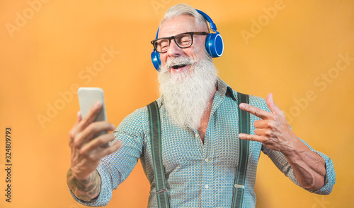 Senior hipster man using smartphone app for creating playlist with rock music - Trendy tattoo guy having fun with mobile phone technology - Tech and joyful elderly lifestyle concept - Focus on face