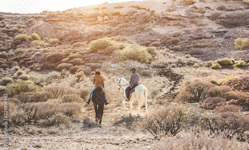 Young people riding horses doing excursion at sunset - Wild couple having fun in equestrian tour  - Training, culture, passion, healthy lifestyle, sport concept