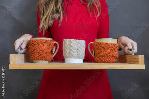 Girl is holding tray with cups in knitted cover with hot drinks.
