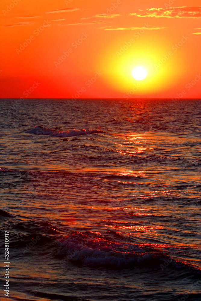 Colorful sunset over the waterline horizon of Baltic Sea with peaceful waves seen from the seaside beach in Karwia resort, north Poland, in summer season