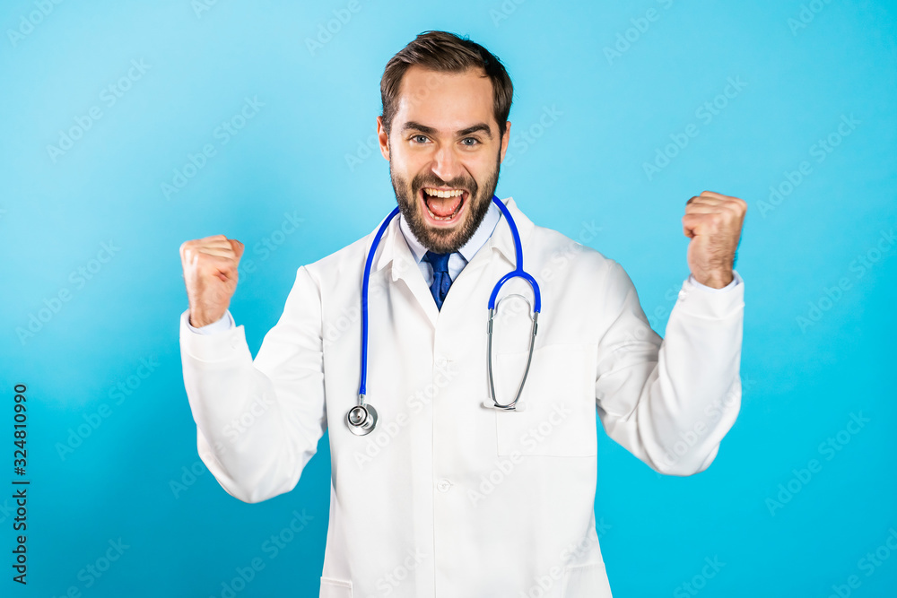 Portrait of happy excited doctor in professional medical white coat showing YES sign gesture. Doc man succeeded at work. Guy isolated on blue background. Portrait of happy excited doctor in professional medical white coat showing YES sign gesture. Doc man succeeded at work. Guy isolated on blue background.