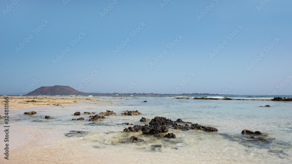 Hot summer views towards the small island of Los Lobos few miles north from Corralejo resort, with calm waves, clear and shallow waters and tropical atmosphere, in Fuerteventura, Canary Islands, Spain