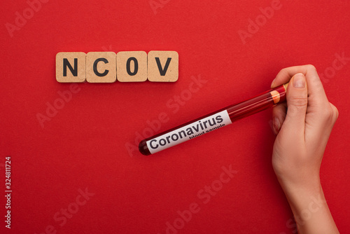 Top view of woman holding test tube with blood sample and coranavirus lettering near wooden cubes with ncov letters on red background photo