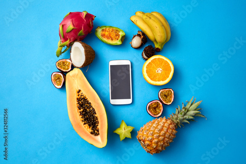 food, diet and healthy eating concept - different exotic fruits around smartphone on blue background