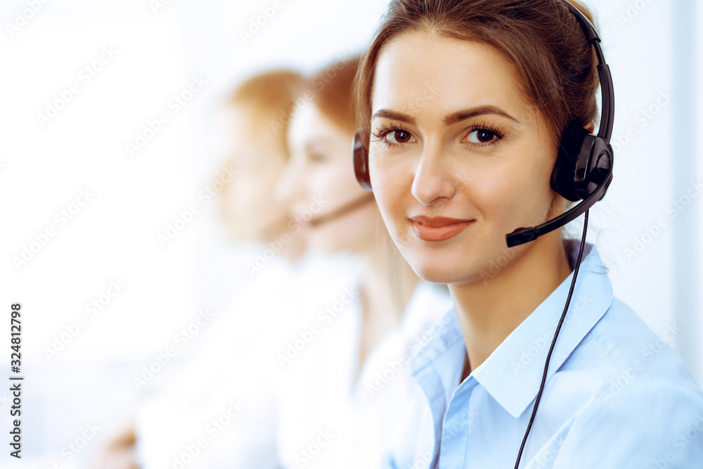 Call center operators. Focus on beautiful business woman using headset in sunny office Call center operators. Focus on beautiful business woman using headset in sunny office