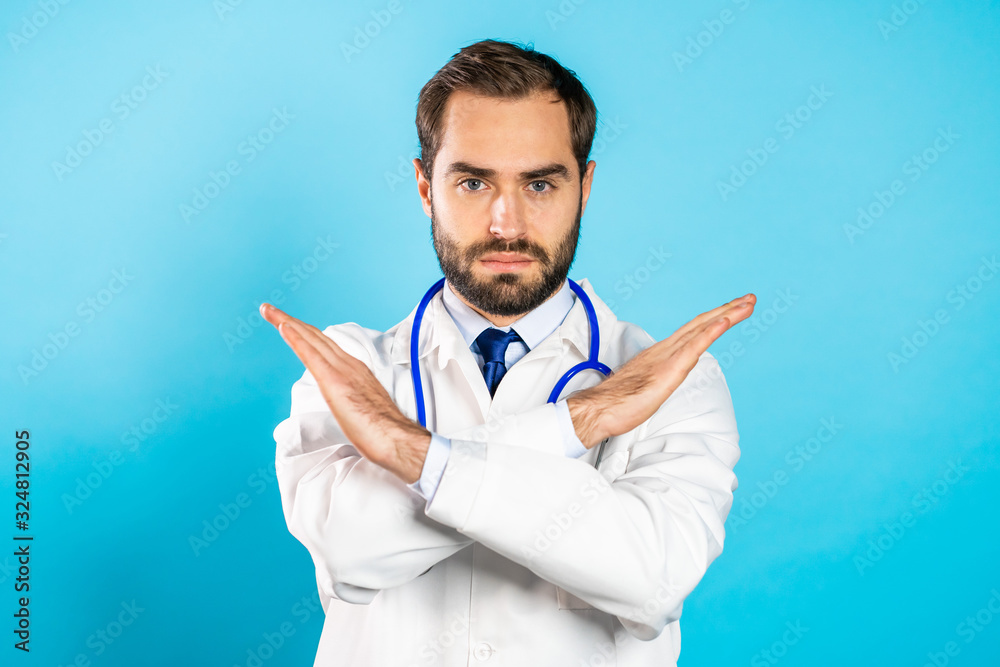 Portrait of serious doctor in professional medical white coat with no crossing hands sign make negation gesture. Denying, Rejecting, Disagree. Doc man isolated on blue background. Portrait of serious doctor in professional medical white coat with no crossing hands sign make negation gesture. Denying, Rejecting, Disagree. Doc man isolated on blue background.