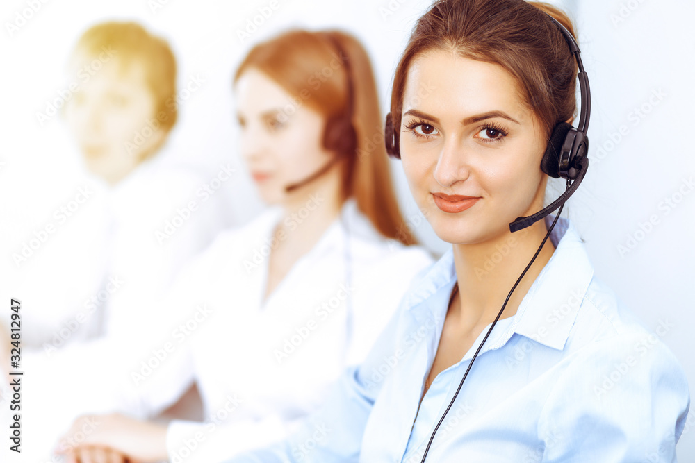 Call center operators. Focus on beautiful business woman using headset in sunny office Call center operators. Focus on beautiful business woman using headset in sunny office