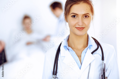 Female doctor smiling on the background with patient in the bed and two doctors photo