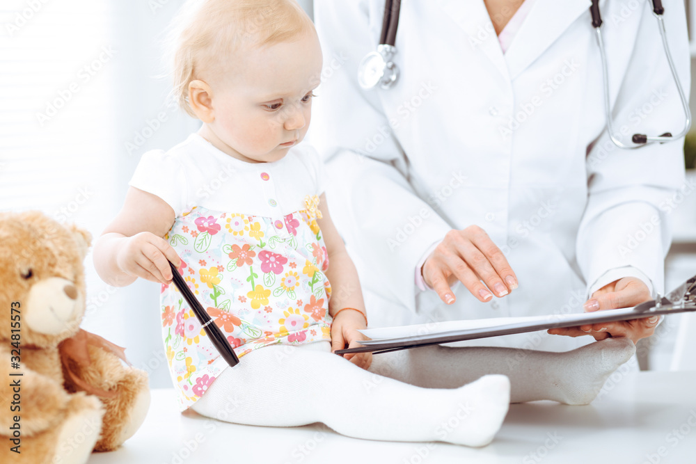 Doctor and patient toddler in hospital. Little girl dressed in dress with pink flowers is being examined by doctor with stethoscope. Medicine concept Doctor and patient toddler in hospital. Little girl dressed in dress with pink flowers is being examined by doctor with stethoscope. Medicine concept