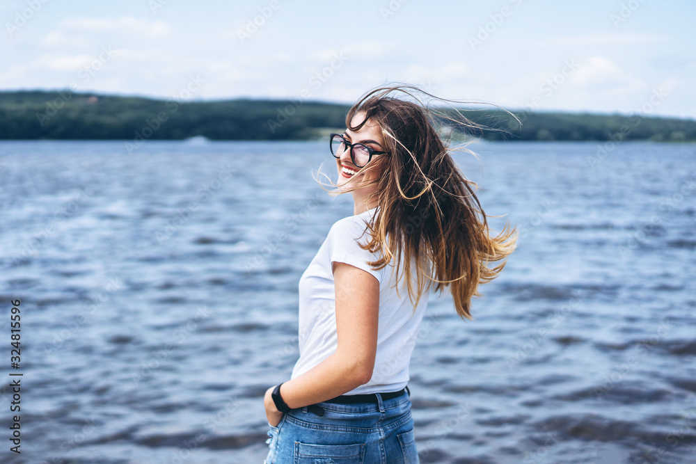 Portrait of a beautiful young woman in stylish glasses. Girl in white tshirt posing on the background of the lake landscape Portrait of a beautiful young woman in stylish glasses. Girl in white tshirt posing on the background of the lake landscape