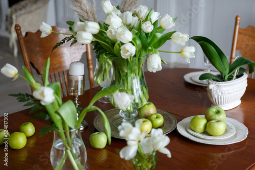 white tulips in a glass vase and green apples on a plate on the table