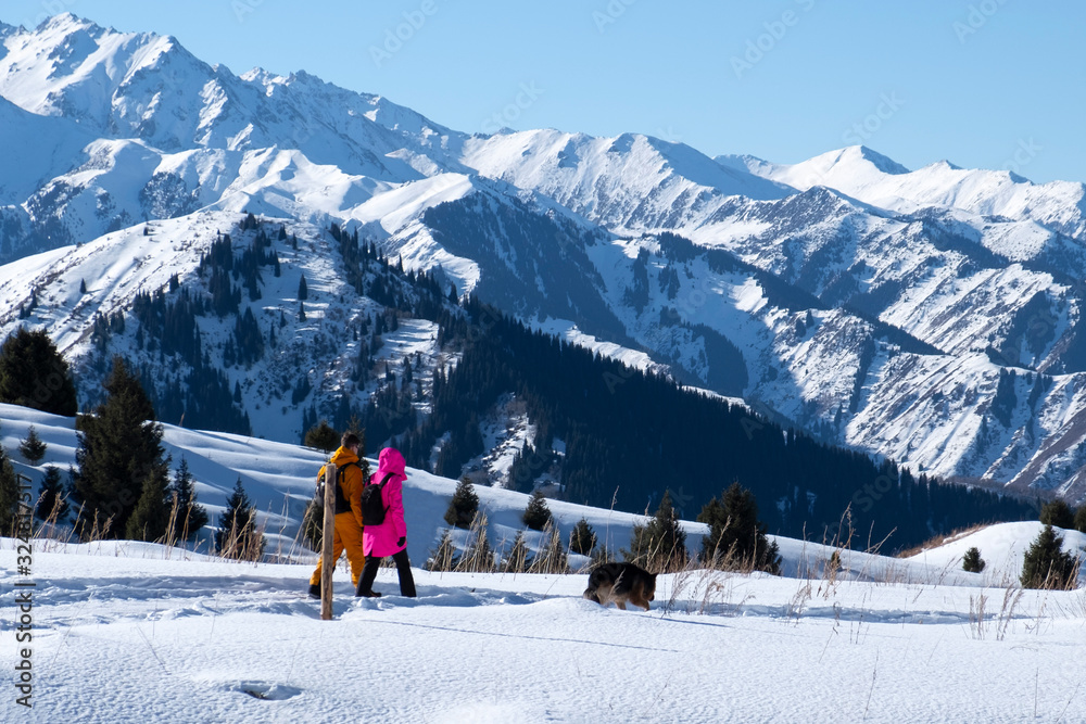 Man and woman are hiking in snow mountains with dog. Trekking in mountains in winter.