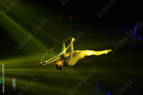Flexible young woman make performance on aerial hoop, yellow light, flexible split on aerial hoop, aerial circus show